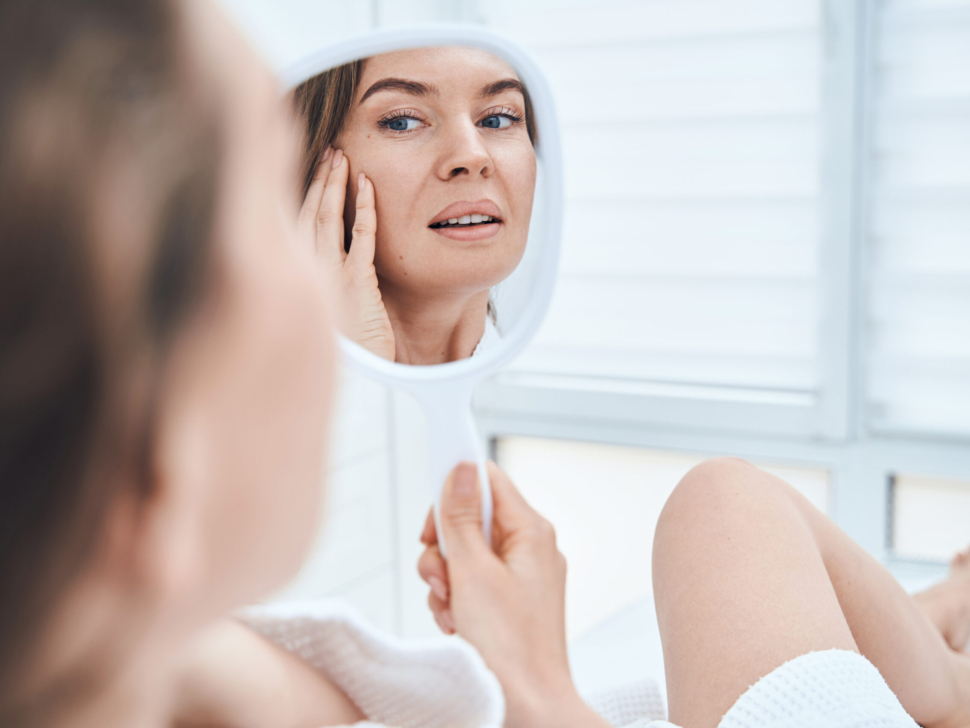 Young cheerful brunette sitting on couch and smiling to her beautiful reflection